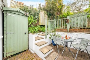 A patio with a table and chairs, a green gate, and a white wall with steps leading up to a wooden deck. - 2 Bed in Appledore (oc-raleig) (Appledore)