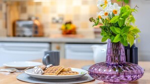A kitchen with a purple vase of flowers on a table, waffles, and a mug.