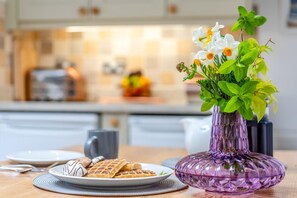 A kitchen with a purple vase of flowers on a table, waffles, and a mug. - 2 Bed in Appledore (oc-raleig) (Appledore)