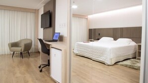 Ein modernes Hotelzimmer mit einem Bett, einem Schreibtisch mit einem Laptop, einem Sessel und einem Fernseher.