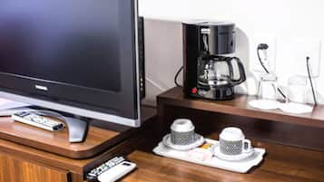 Un televisor, una cafetera y dos tazas sobre una mesa de madera.