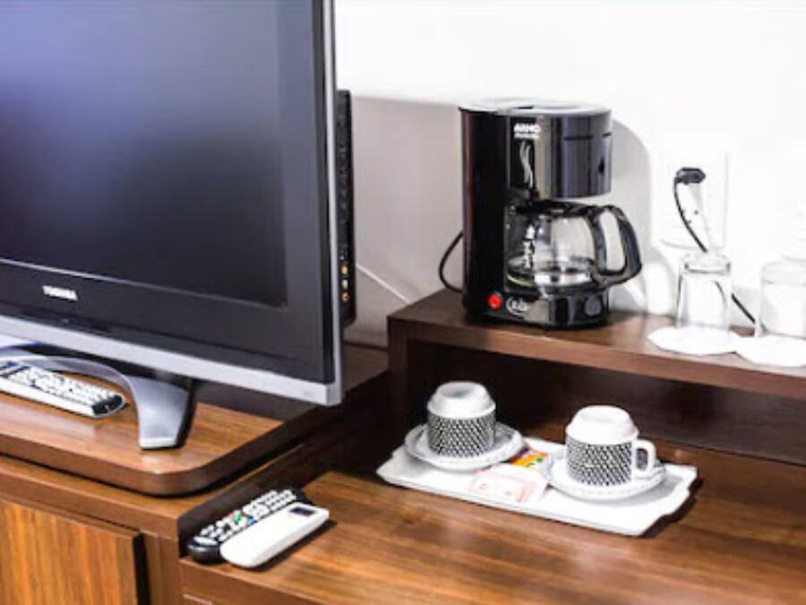 Un televisor, una cafetera y dos tazas sobre una mesa de madera.
