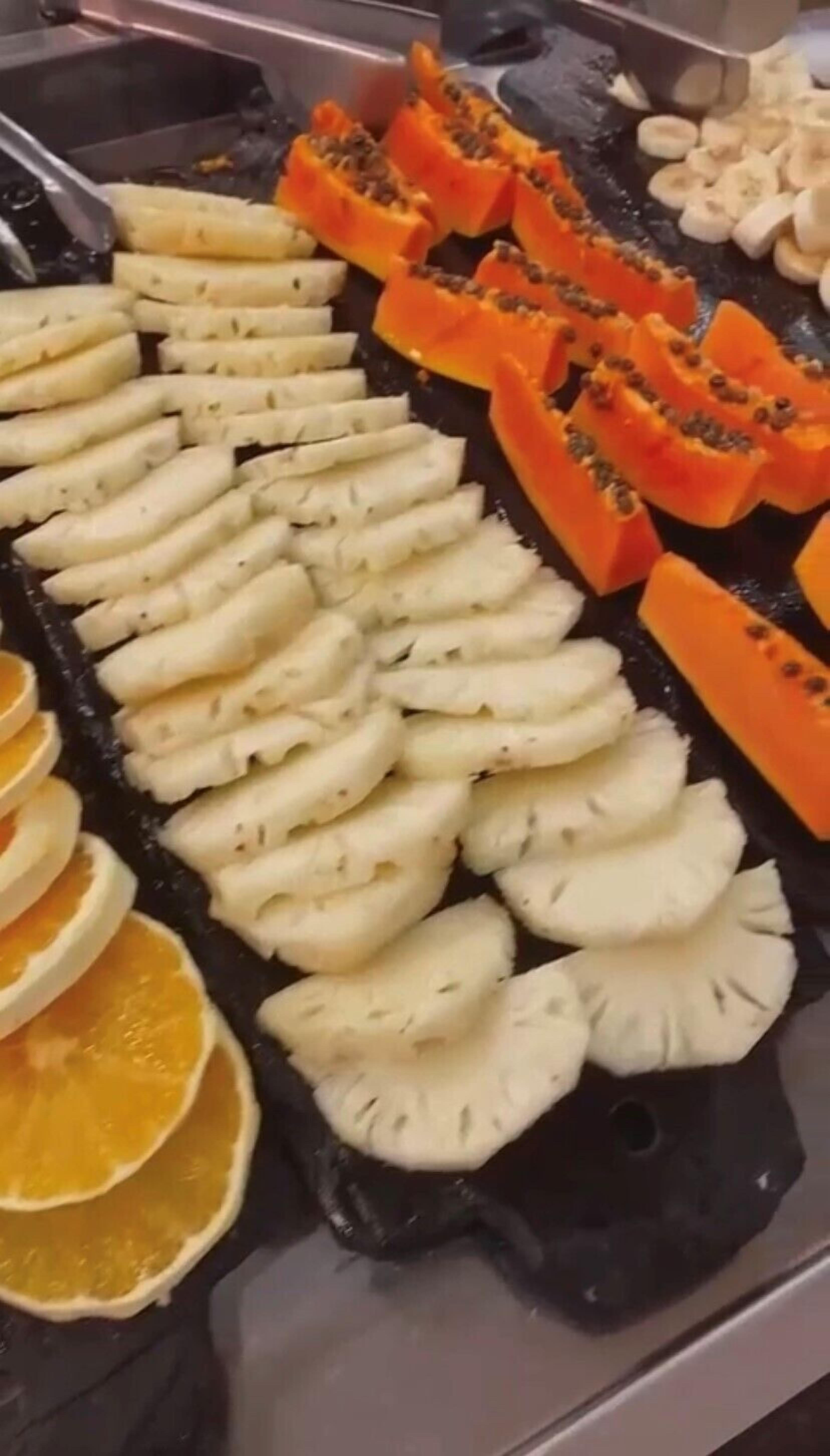 Een buffet met gesneden fruit, zoals papaya, bananen en ananas.