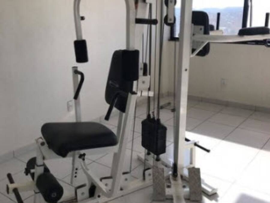 A gym with a bench, weight machines, and a window with a view of the city.