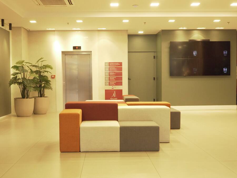 A modern lobby with a sectional sofa, potted plants, a wall-mounted TV, and directional signs.