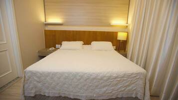 A hotel room with a large bed, two bedside tables, a nightstand, and a lamp.