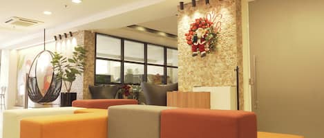 Un área de espera moderna con asientos acolchados, un muro decorativo y un amplio ventanal que proporciona luz natural.