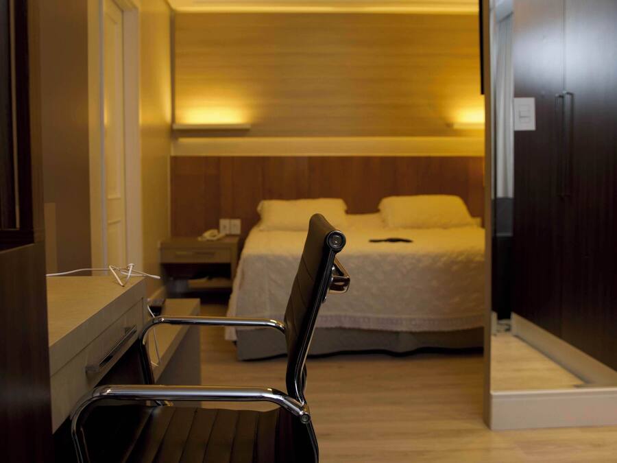 Una habitación de hotel con cama, mesita de noche, silla y aire acondicionado.