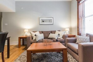 A living room with a brown sofa set, two side tables with lamps, a wooden coffee table, and a framed picture on the wall. - Windy City Wanderer - Depaul, Train, Wrigley Field (Chicago)