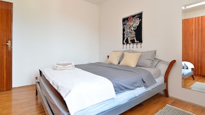 Una cama bien tendida con edredón gris y blanco, almohadas y una toalla blanca doblada al lado.