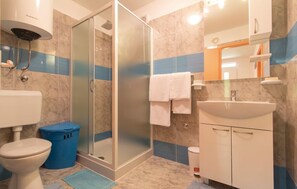 Une salle de bain avec une douche à parois de verre, des toilettes, un lavabo et une poubelle.