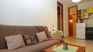 A living room with a sofa, a coffee table, a lamp, and a kitchen area with cabinets and a refrigerator. - Apartment 397 (Pula)