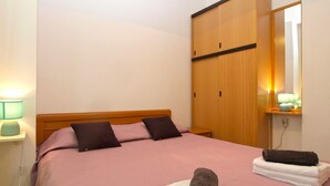 A bedroom with a bed, a wooden wardrobe, a nightstand with a lamp, and a mirror. - Apartment 397 (Pula)