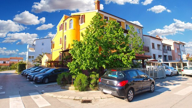 A yellow building with a tree in front, parked cars, and a clear blue sky. - Apartment 397 (Pula)