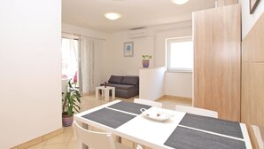 A modern living room with a sofa, a dining table with chairs, a potted plant, and a window with curtains. - Apartment 1406 (Pula)