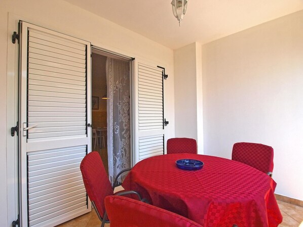 Un coin repas comprenant une table et quatre chaises, une nappe rouge et une porte équipée de stores horizontaux.