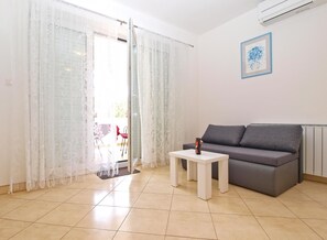 Una sala de estar con un sofá gris, una mesita blanca y un ventanal que da a un espacio exterior.