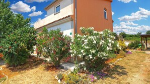 A two-story house with a beige and orange facade, surrounded by a garden with various flowering plants and trees. - Apartment 1406 (Pula)
