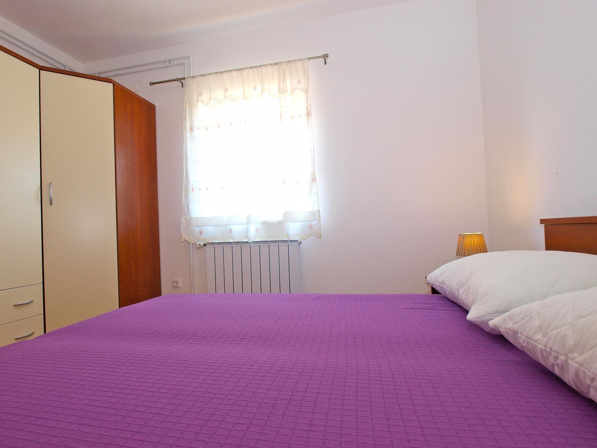 A bedroom with a bed, a wardrobe, a window with a curtain, and a radiator.
