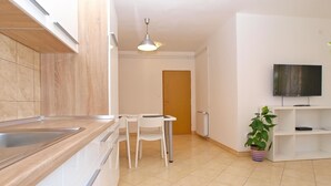 A modern kitchen with white cabinets, a wooden countertop, and a dining area with a table and chairs. - Apartment 1406 (Pula)