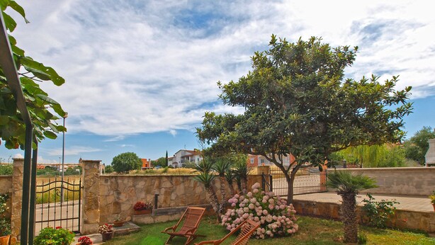 Un jardin bien entretenu, agrémenté d’un mur en pierre, de deux chaises longues en bois et de diverses plantes en pot.