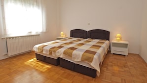 Une chambre à coucher avec un lit double, deux tables de chevet avec des lampes, un radiateur et une fenêtre avec des rideaux.