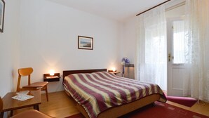 Un dormitorio con una cama, una silla, una mesita pequeña y una mesita de noche con una lámpara.