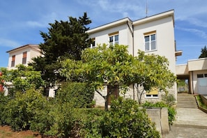 Un edificio moderno de dos pisos con techo plano y un gran árbol en el jardín delantero.