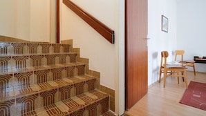 Una escalera con baldosas estampadas, barandilla de madera y una puerta que da a una habitación con un escritorio y sillas.