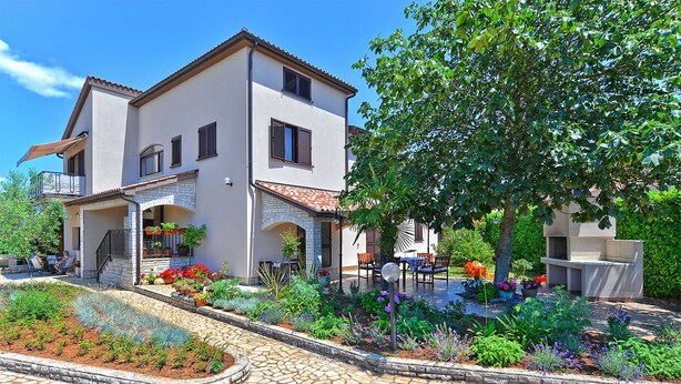 A two-story house with a patio area, outdoor seating, and a garden with various plants and flowers. - Apartment 38 (Fazana)