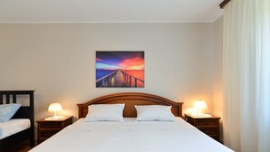 A hotel room with a large bed, two bedside tables with lamps, a nightstand, a wooden headboard, and a painting of a sunset over a pier on the wall. - Apartment 38 (Fazana)