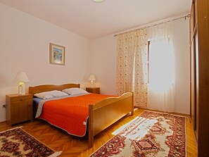 A bedroom with a wooden bed, two bedside tables with lamps, a framed picture on the wall, and a patterned rug on the floor.