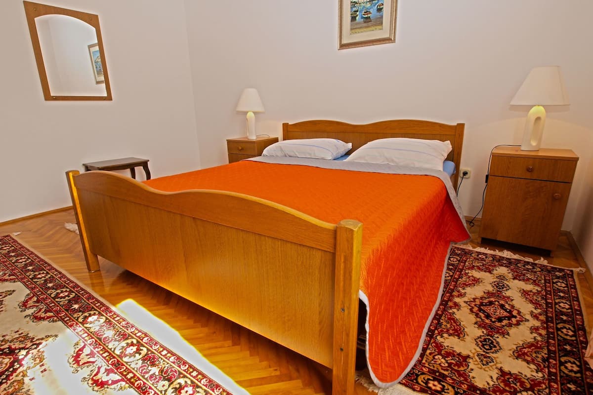 A bedroom with a wooden bed, two bedside tables, a nightstand, a mirror, and a painting on the wall.