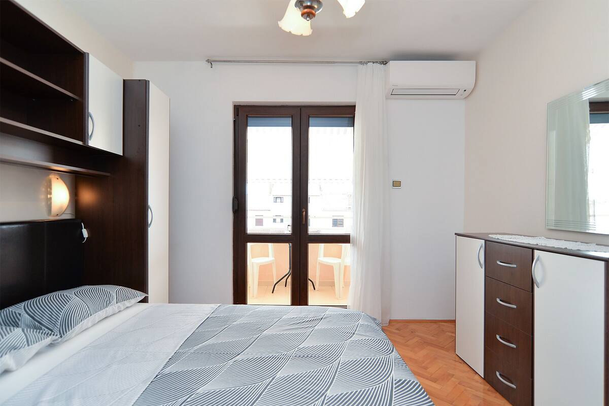 Un dormitorio con cama, armario, escritorio y ventana con vistas a edificios.