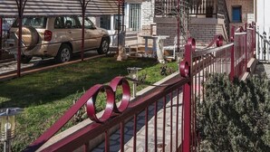 Un immeuble résidentiel à structure de deux étages, doté de balcons ornés de plantes, d’une voiture garée et d’une rambarde rouge.