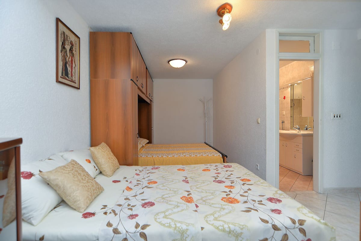 Un dormitorio con cama, un armario de madera, una lámpara en el techo y un baño visible a través de una puerta abierta.