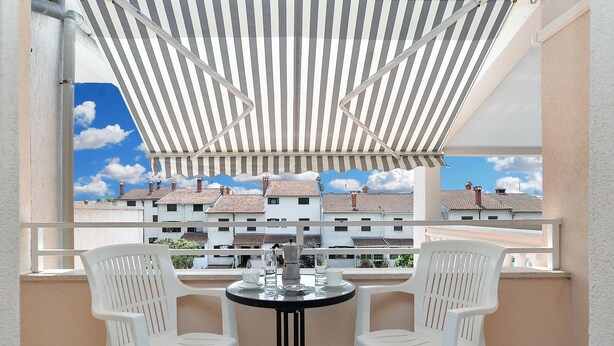 Un balcon avec deux chaises en plastique blanches, une petite table ronde et un auvent à rayures.
