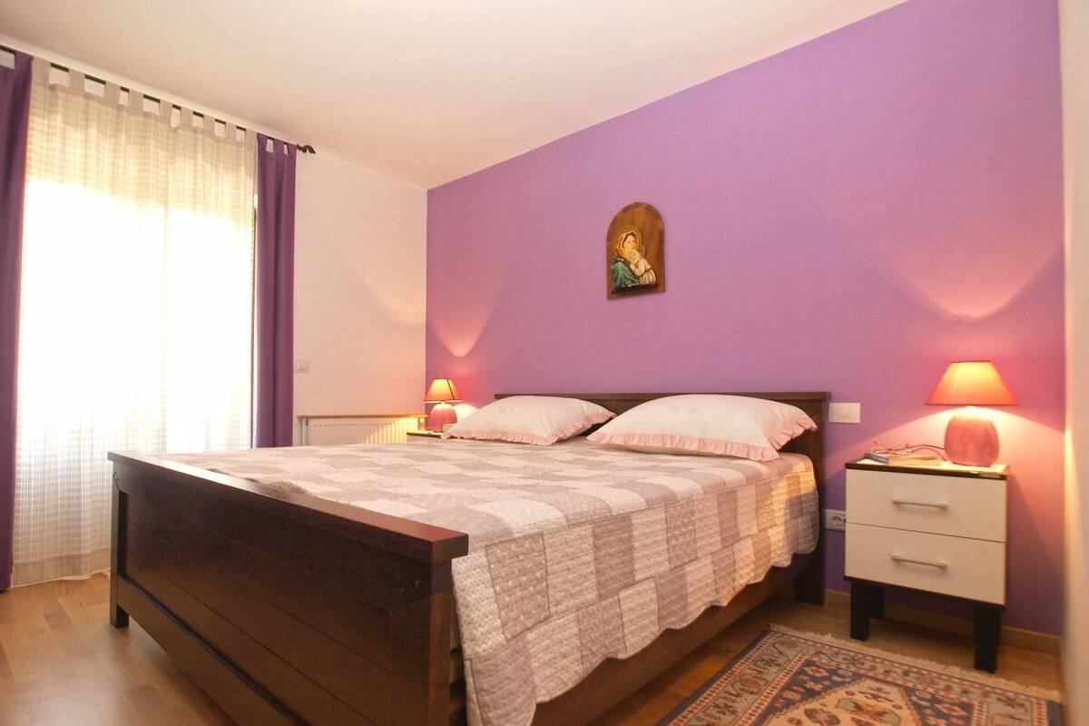 A bedroom with a bed, nightstands, a lamp, a wall decoration, and a patterned rug.