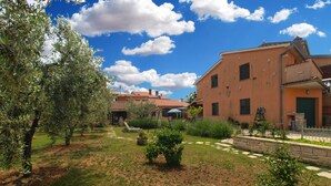 A courtyard with a stone pathway, olive trees, and a building with a red-tiled roof. - Apartment 64 (Vodnjan)