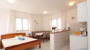 A hotel room with a bed, a small dining table, a sofa, a kitchen area with a coffee machine, and a trash bin. - Apartment 72 (Pula)