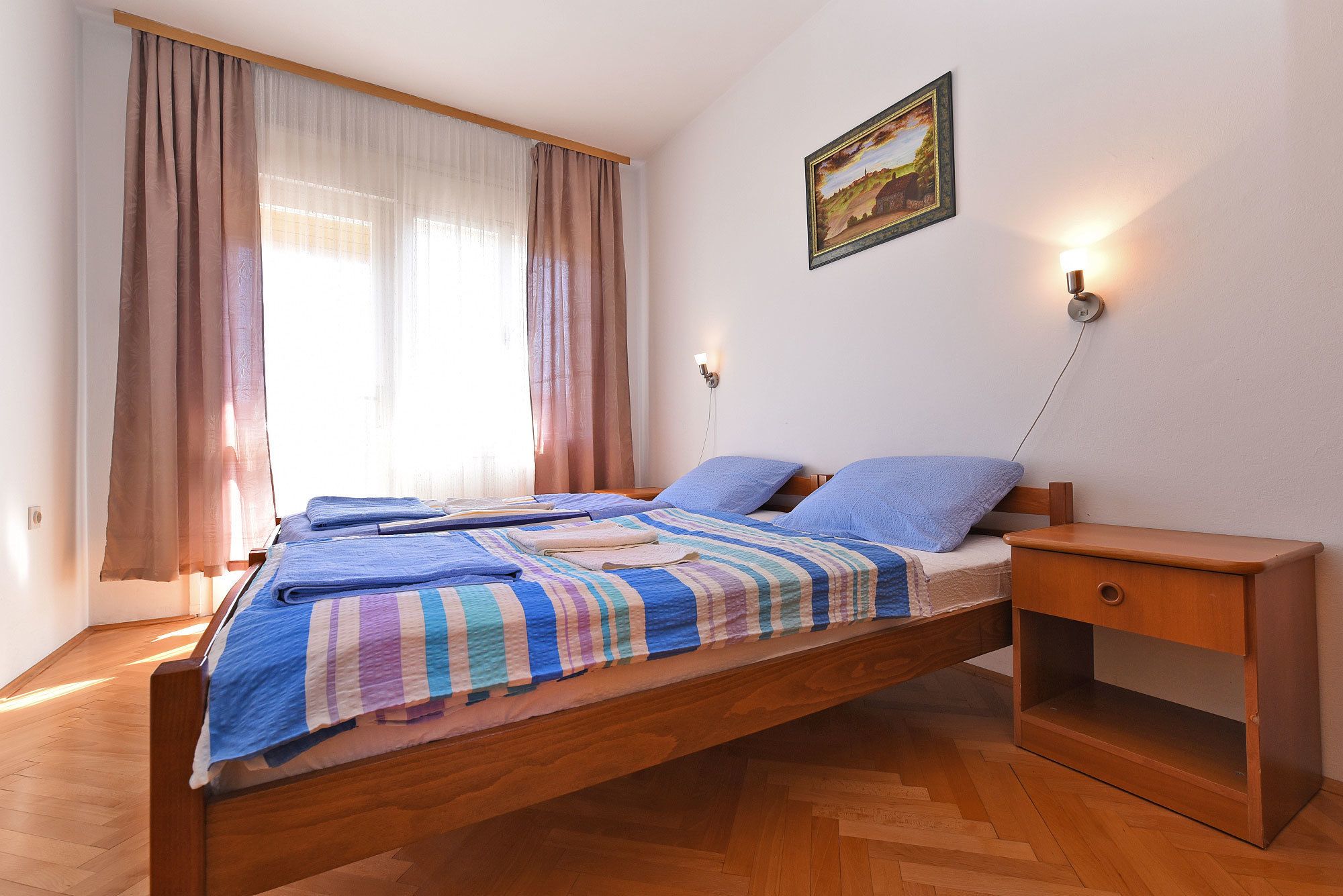 Un dormitorio con cama de madera, dos almohadas, una mesita de noche y una lámpara de pared.
