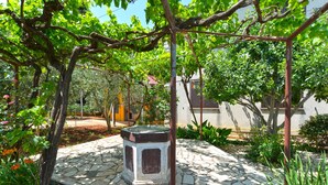 Un giardino con una fontana in pietra, circondato da vegetazione e un edificio sullo sfondo.