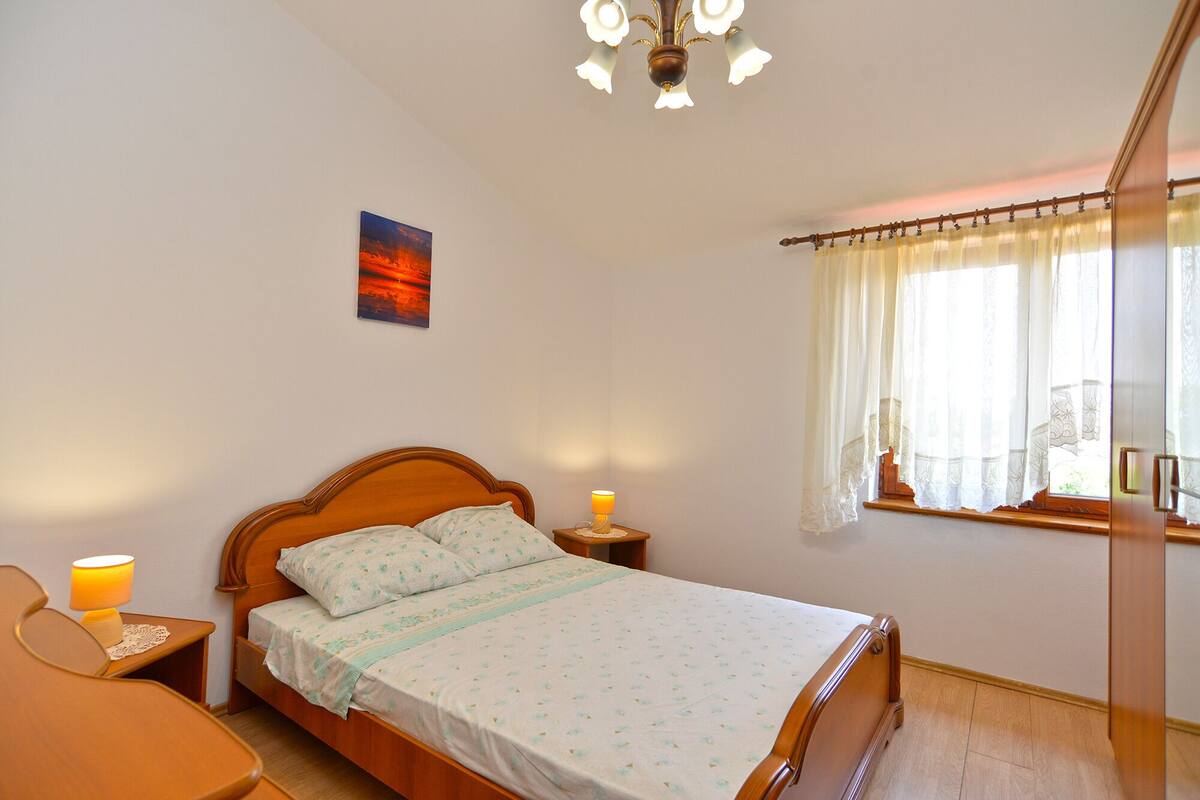A neatly arranged bedroom with a bed, bedside lamps, a nightstand, a window with curtains, and a painting on the wall.