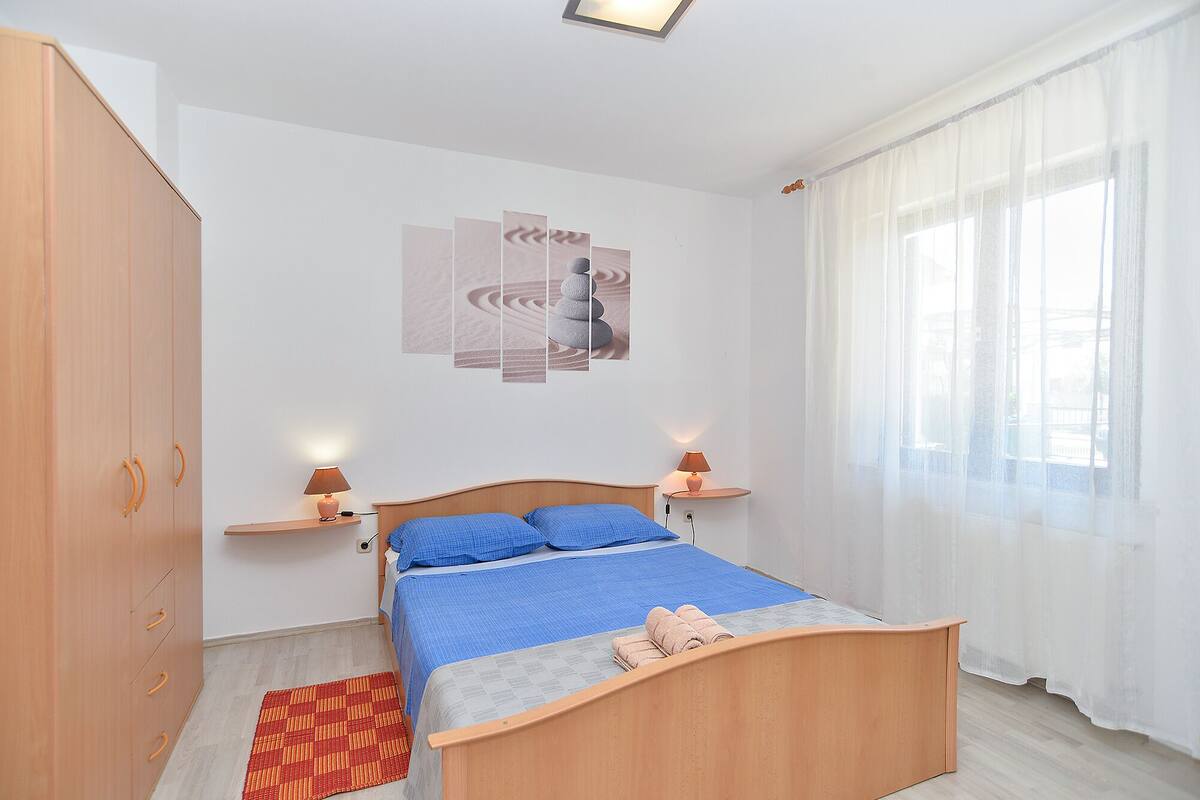 A bedroom with a bed, bedside lamps, a wall art piece, and a window with curtains.