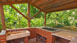 Un espace barbecue extérieur en briques, équipé d’un évier et d’une table, et entouré d’arbres.