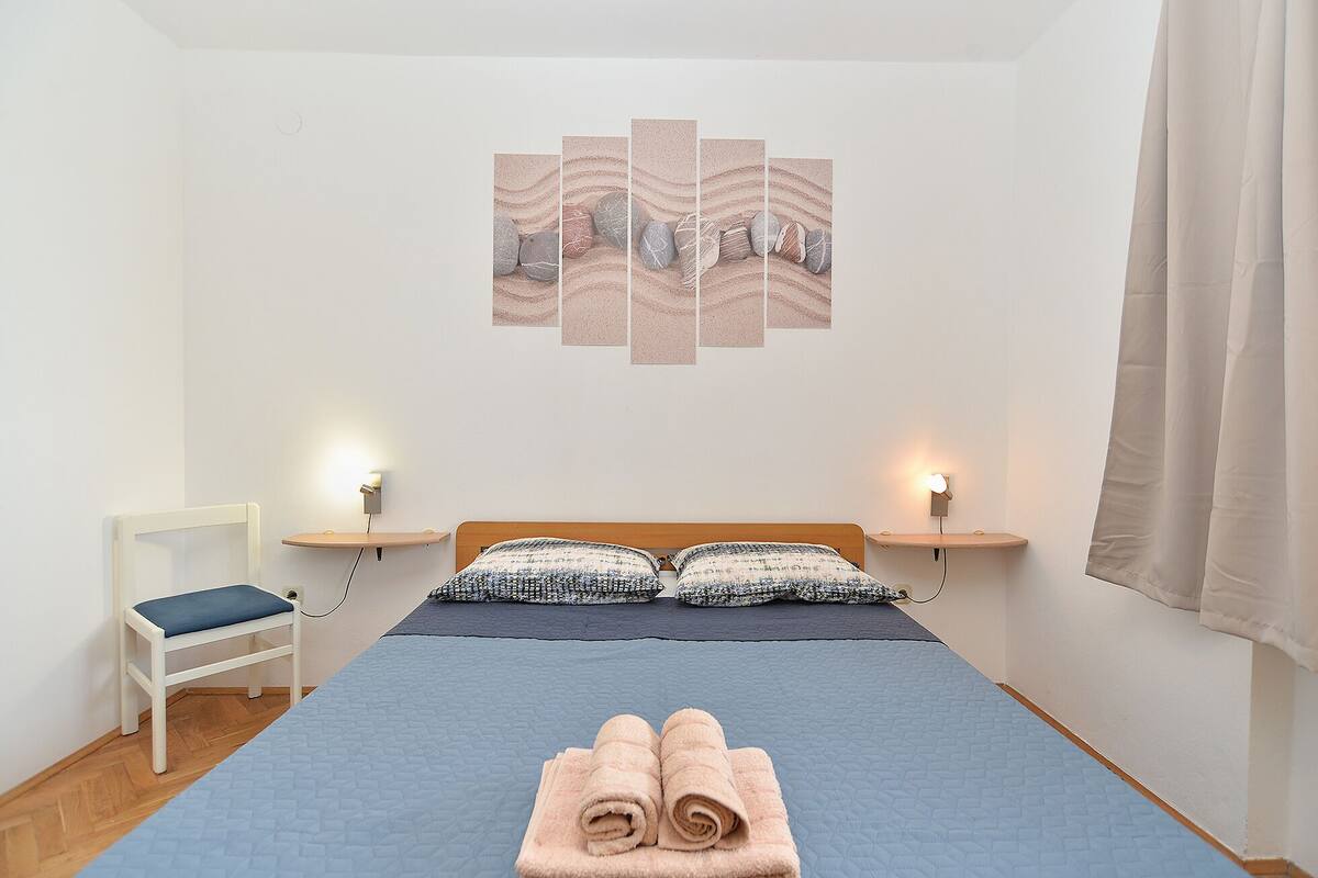 A bedroom with a bed, two bedside tables, a chair, and a wall art piece.
