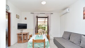Un salon avec un canapé, une table à manger et des chaises, un téléviseur et une fenêtre avec des rideaux.