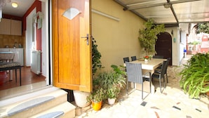 Un espace patio doté d’une porte en bois, de sièges d’extérieur, de plantes en pot et d’un sol carrelé.