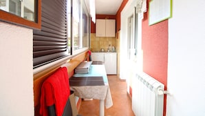 Un couloir étroit mène à une cuisine équipée d’une fenêtre, d’un radiateur et d’une table avec un banc.
