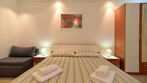 A hotel room with a bed, two bedside lamps, a nightstand, a small sofa, and a painting on the wall.